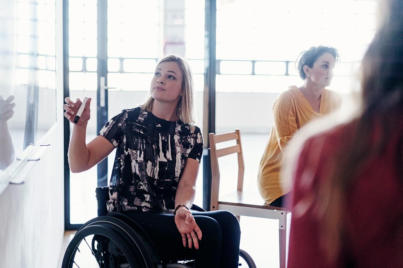 Confident disabled businesswoman giving a presentation. She is holding a felt tip pen while looking at a whiteboard.