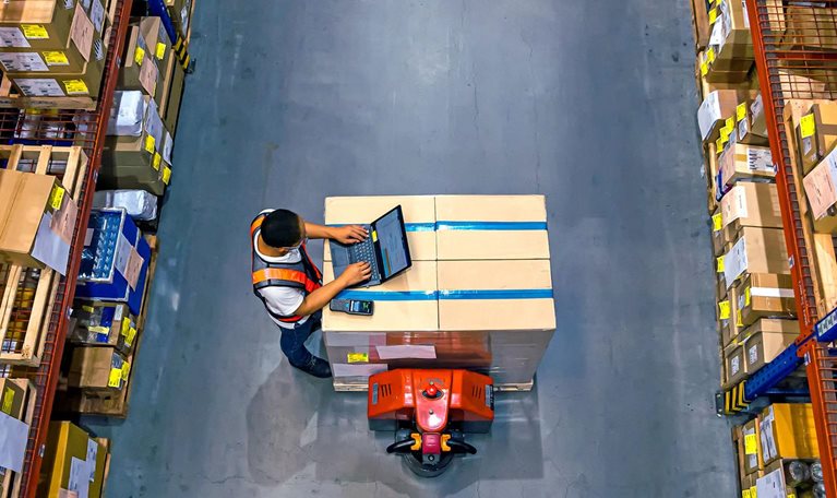 Top view of warehouse worker using laptop to check location of goods