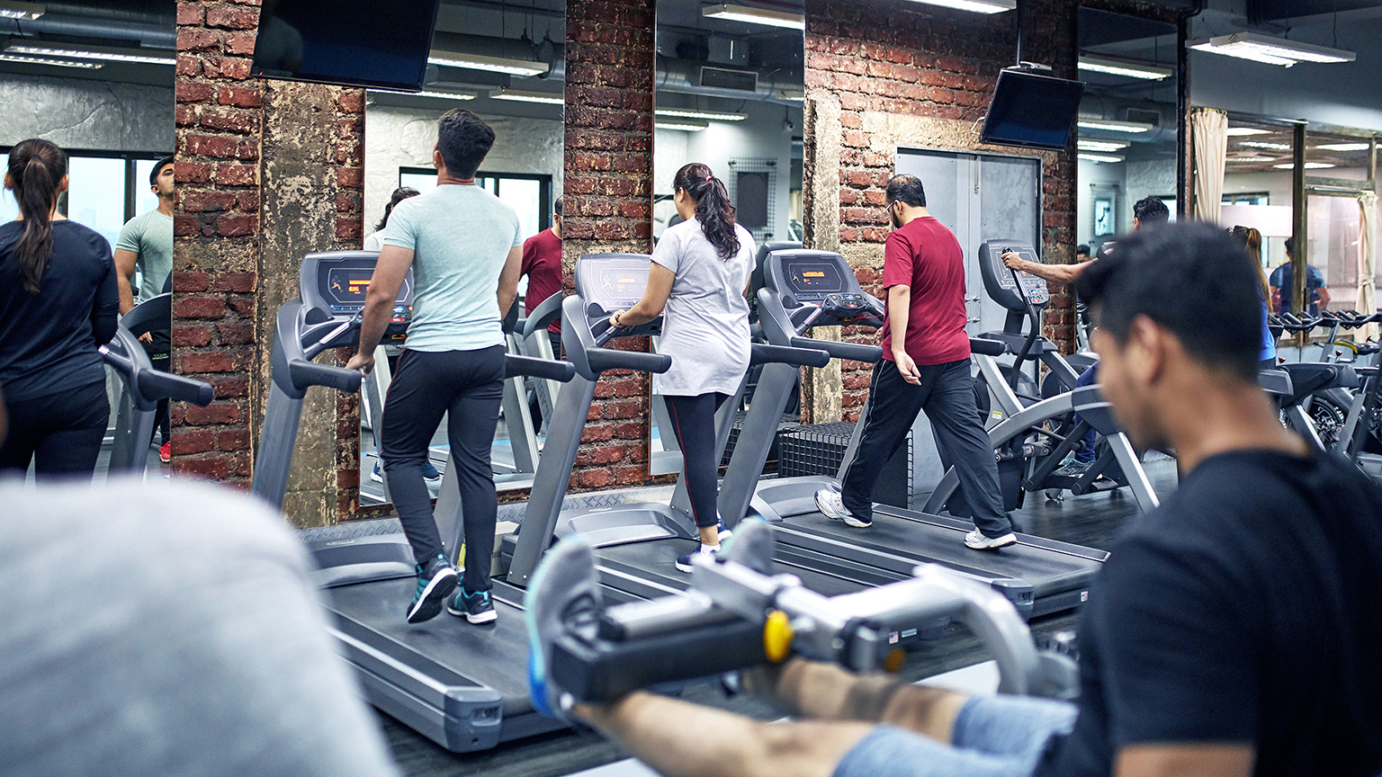 People using treadmills and workout equipment in a modern fitness center in India.