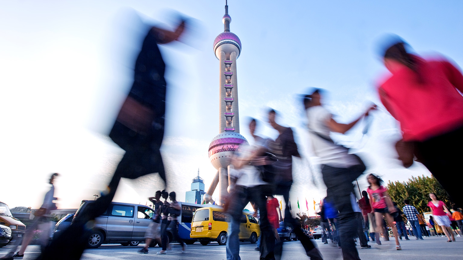From a low angle, pedestrians are seen hurrying by with the Shanghai Oriental Pearl Tower standing prominently in the background.