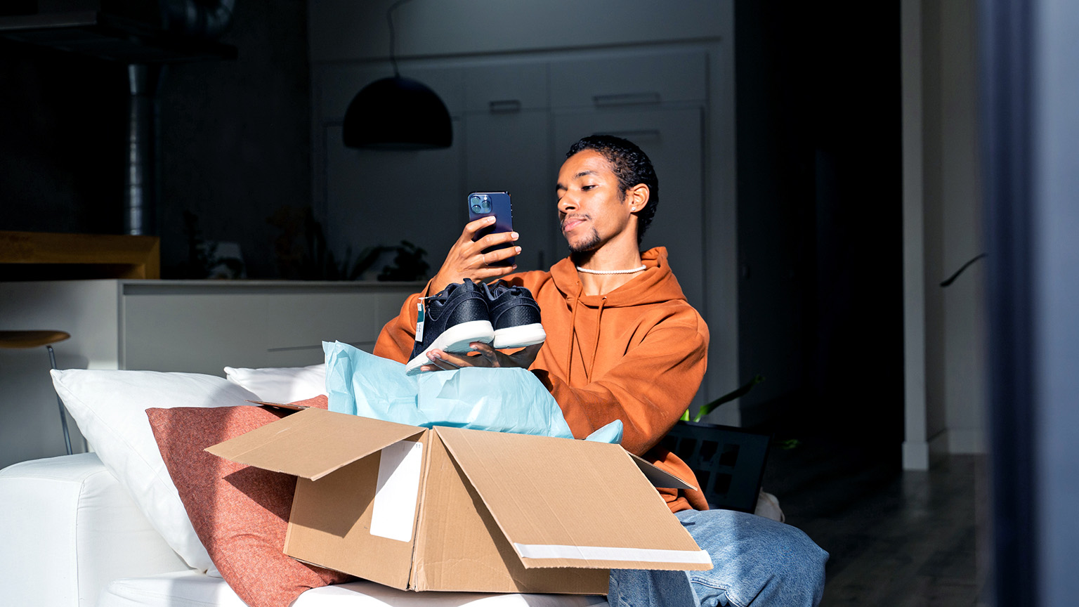 A young man lifts up a pair of new sneakers from a delivery box in order to capture an image for social media.