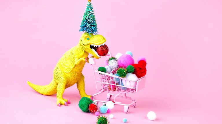 A festive image of a toy dinosaur wearing a Christmas tree on its head and filling a shopping cart with multicolored puff balls.