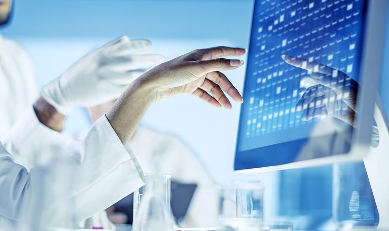 Close up image of scientists discussing and gesturing with their hands at data on a monitor.