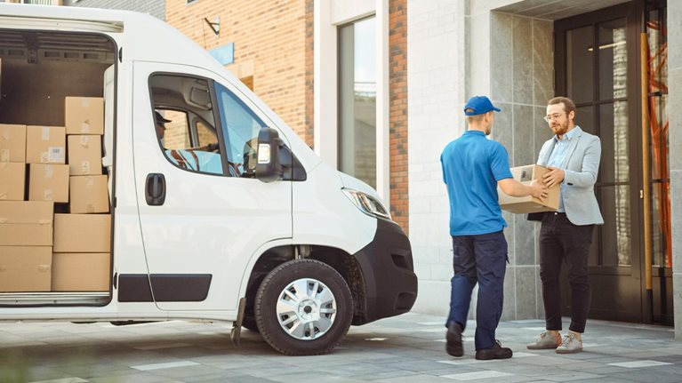 In stylish modern urban office area courier delivers cardboard box parcel to a man - stock photo